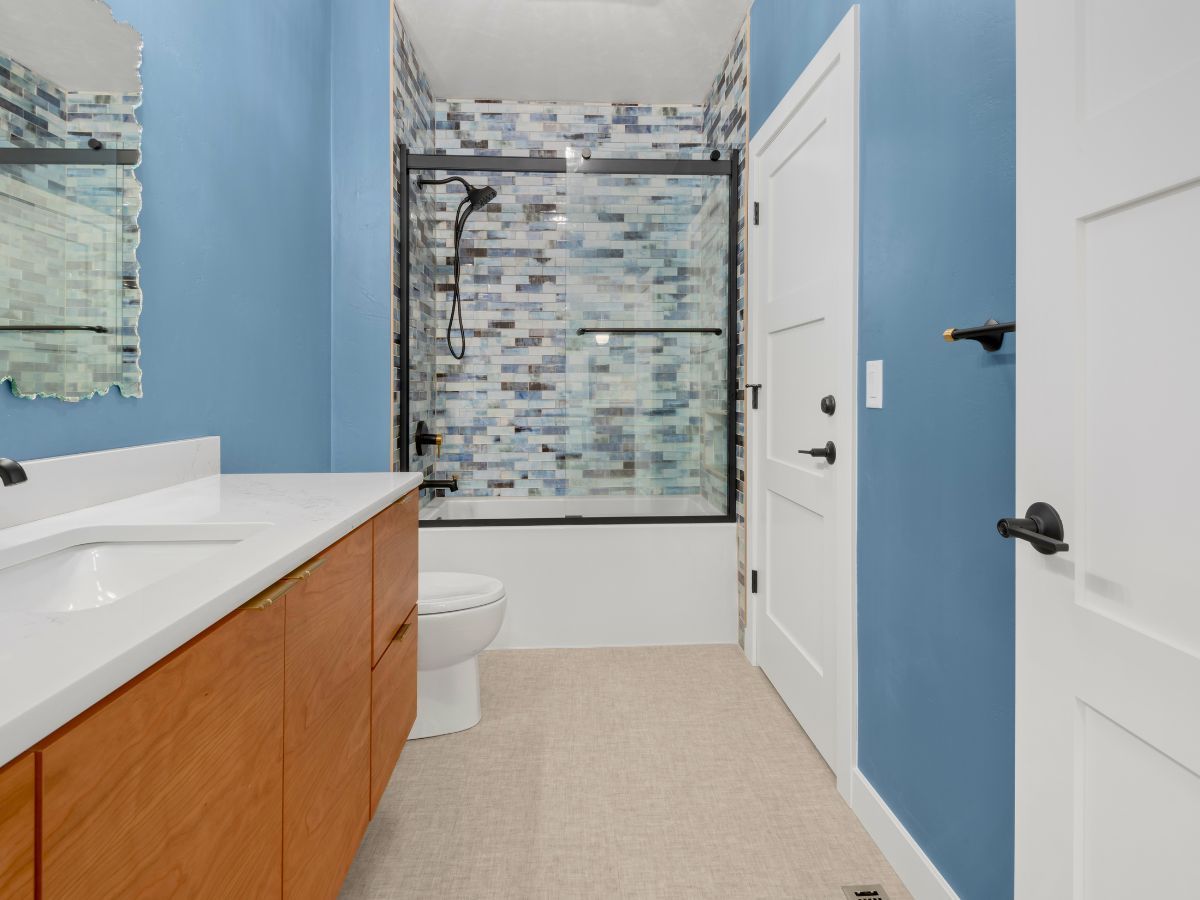 A bathroom with blue walls , a toilet , sink and shower.
