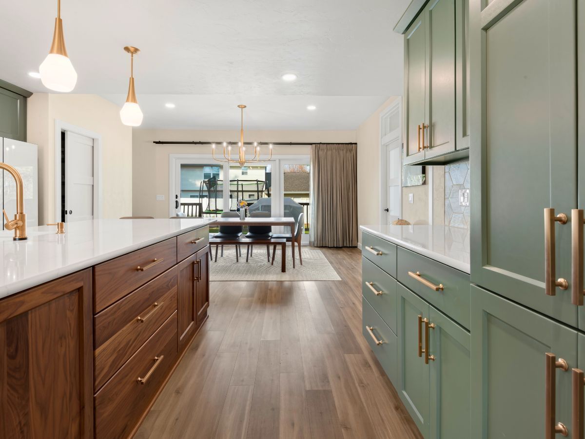 A kitchen with green cabinets and wooden cabinets and a dining room in the background.