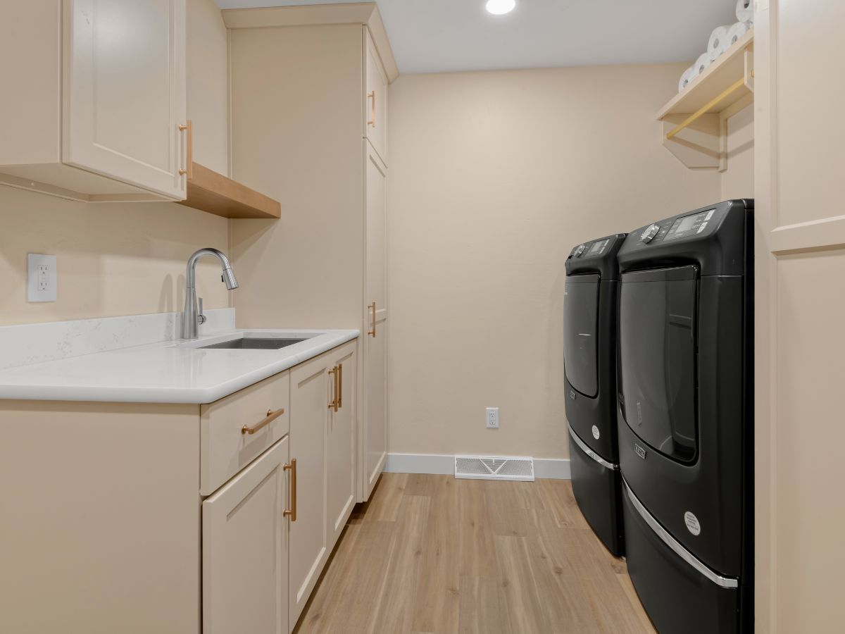 A laundry room with two black washers and dryers and a sink.