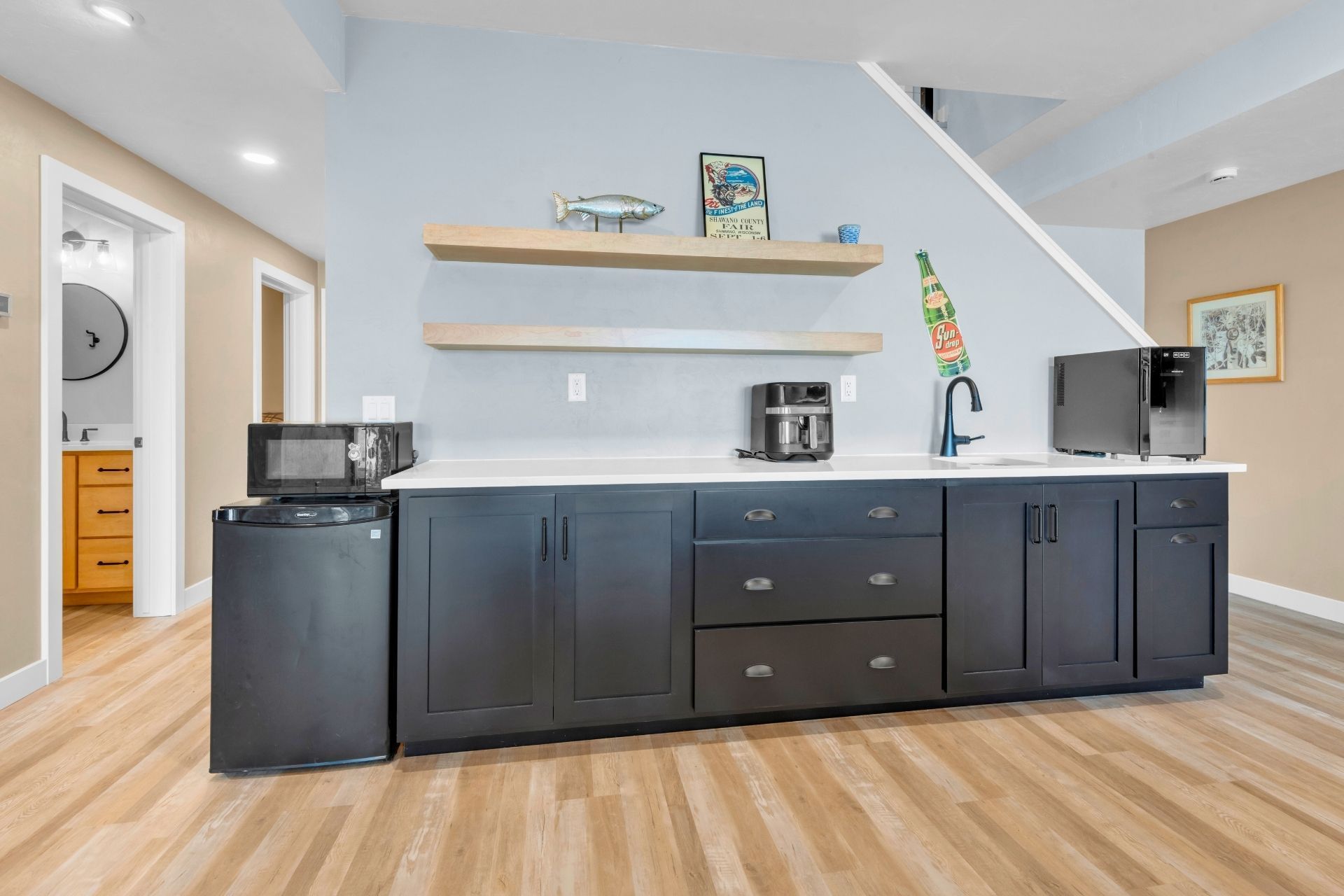 A kitchen with black cabinets , a black refrigerator , a microwave , and a coffee maker.