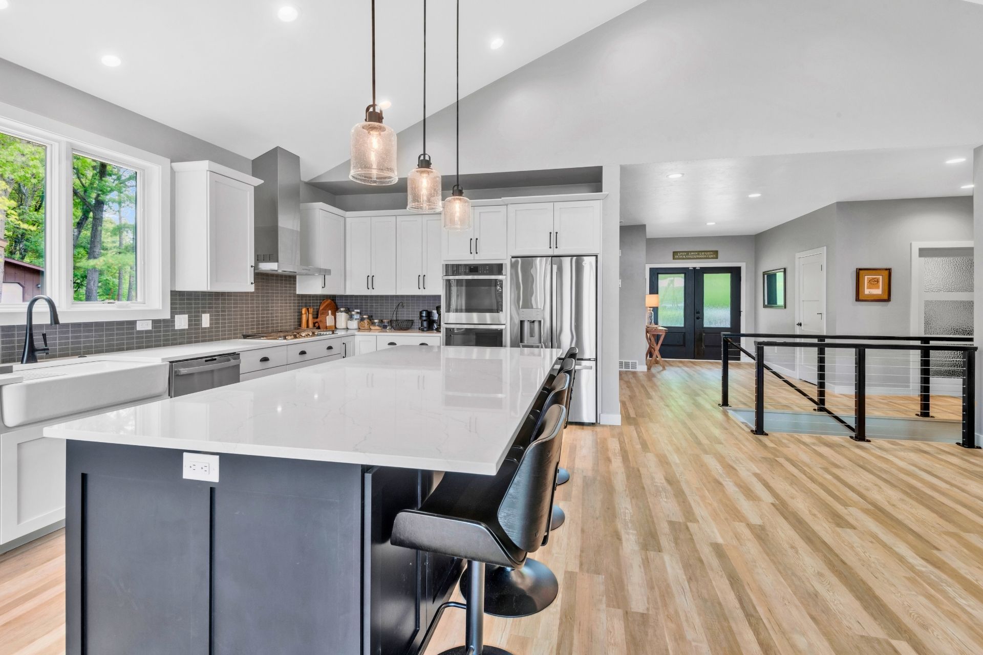 A kitchen with a large island , white cabinets , stainless steel appliances and hardwood floors.
