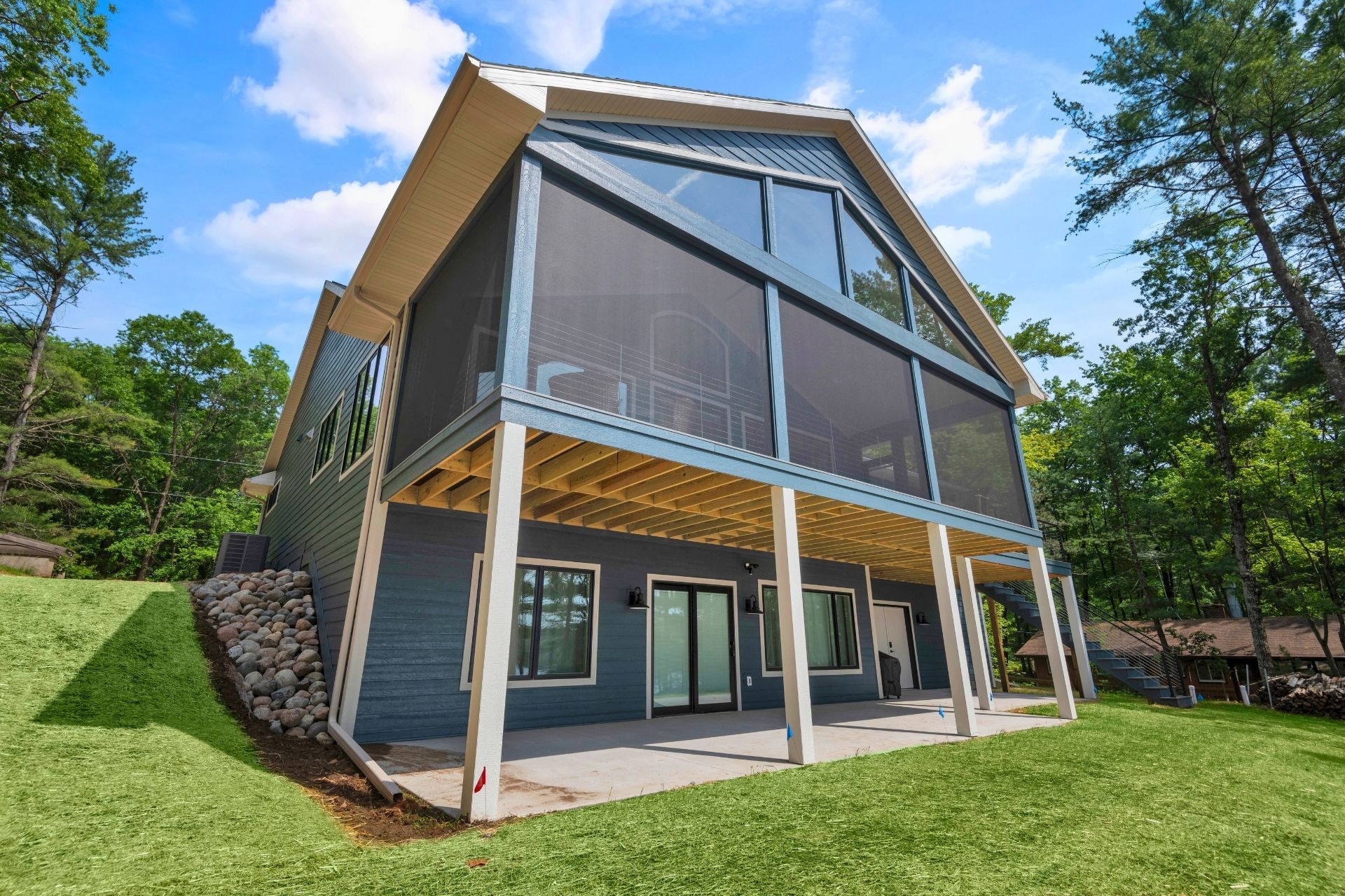 A large house with a screened in porch is sitting on top of a lush green hillside.
