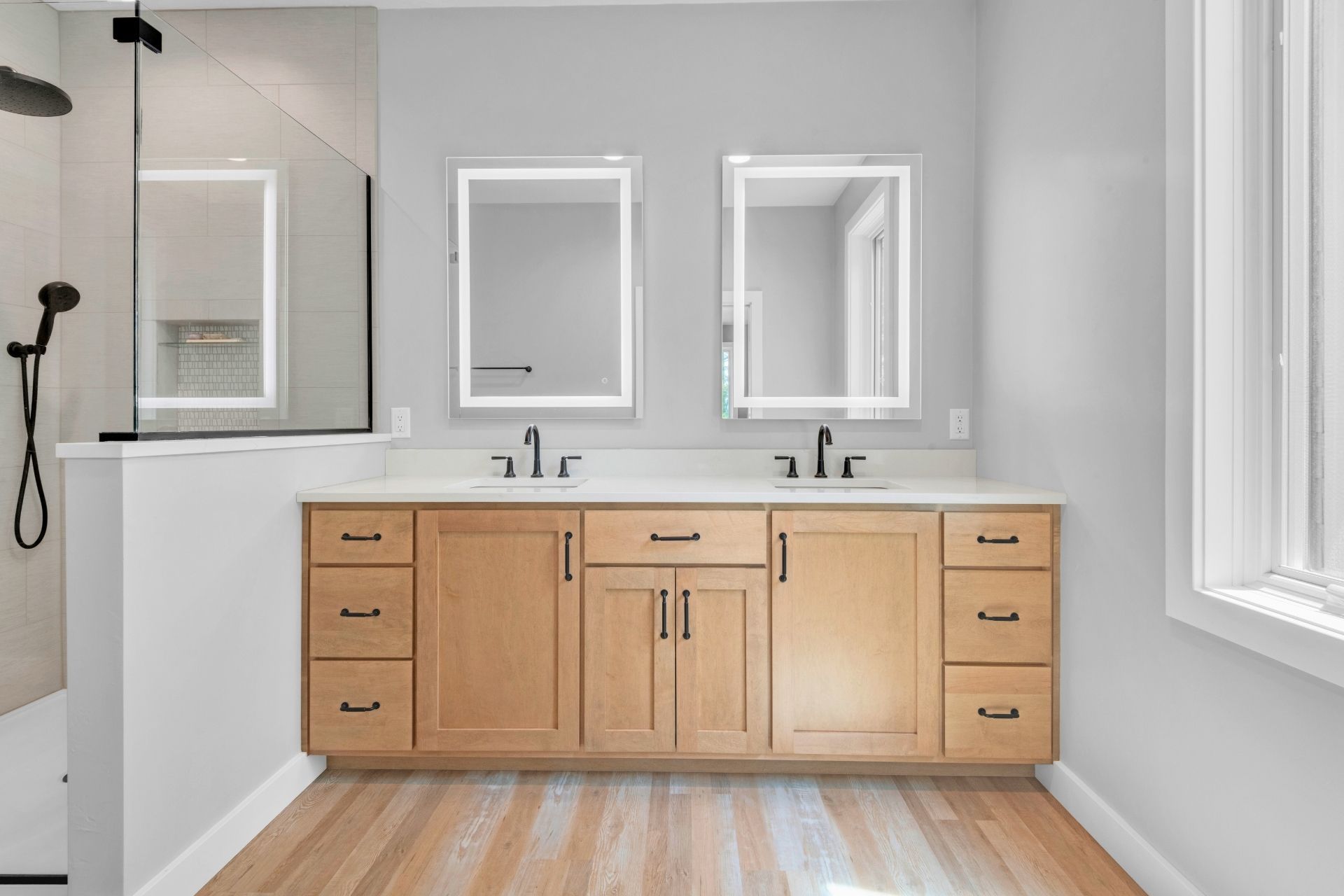 A bathroom with two sinks , two mirrors and a walk in shower.