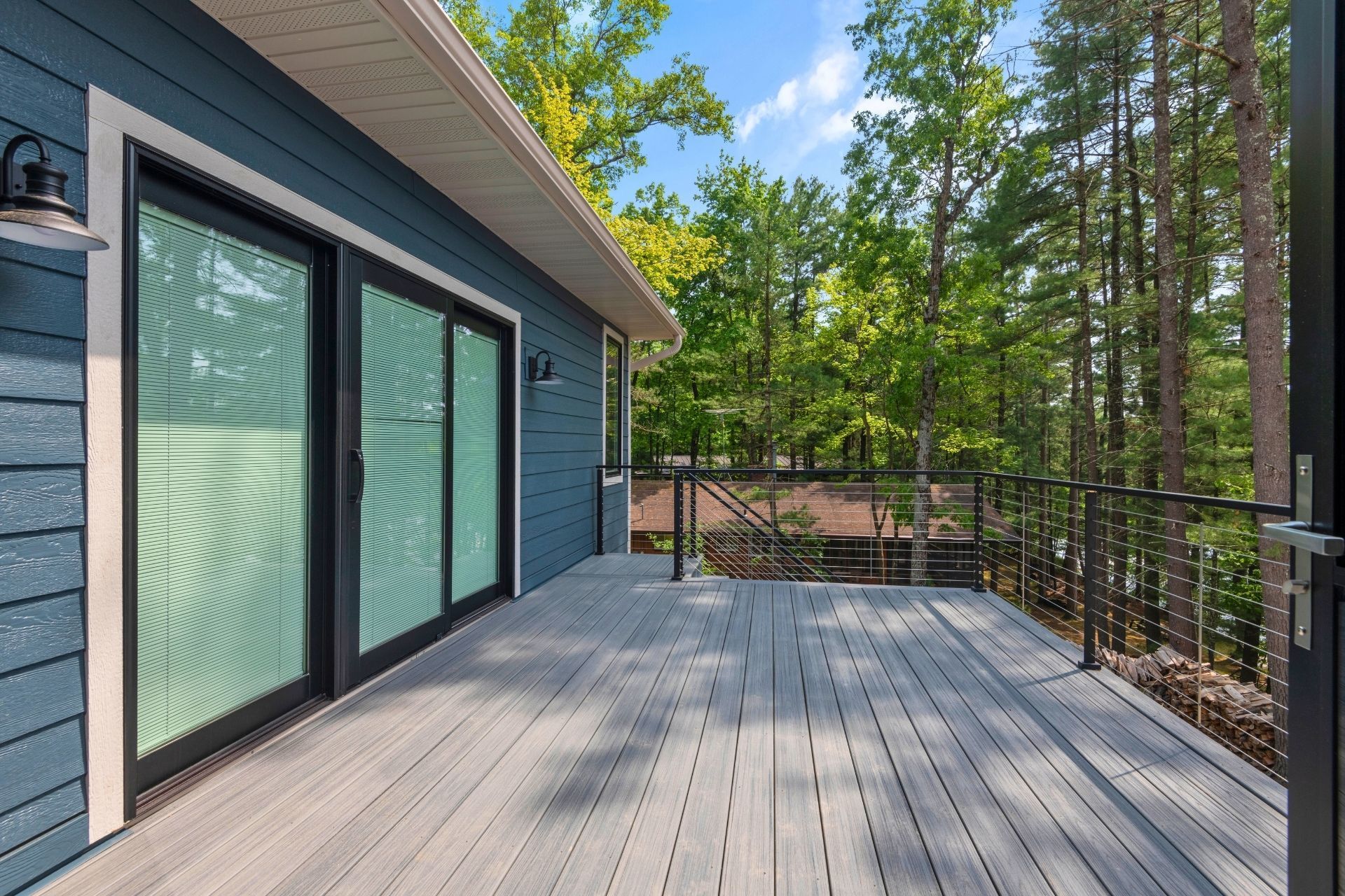 A large deck with sliding glass doors is surrounded by trees.