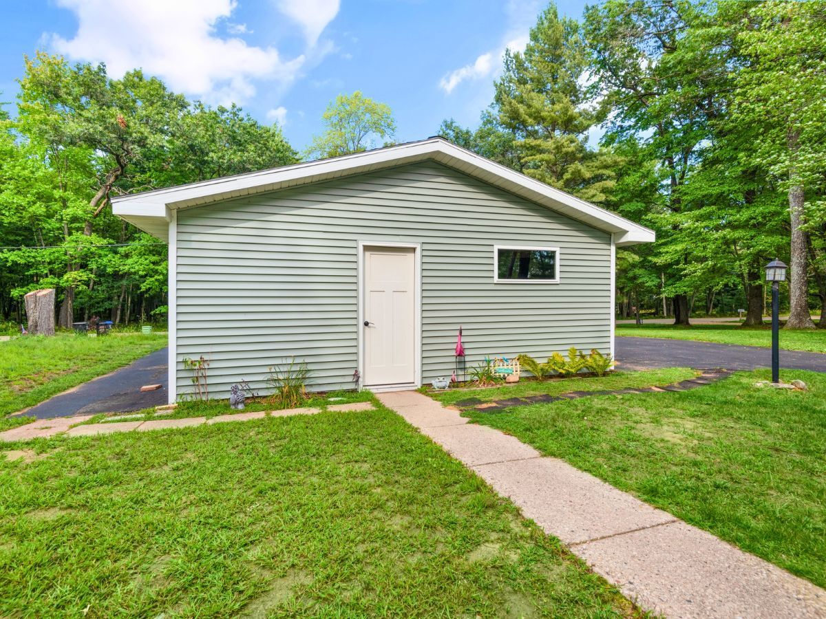 A small white garage with a white door is sitting in the middle of a lush green field.