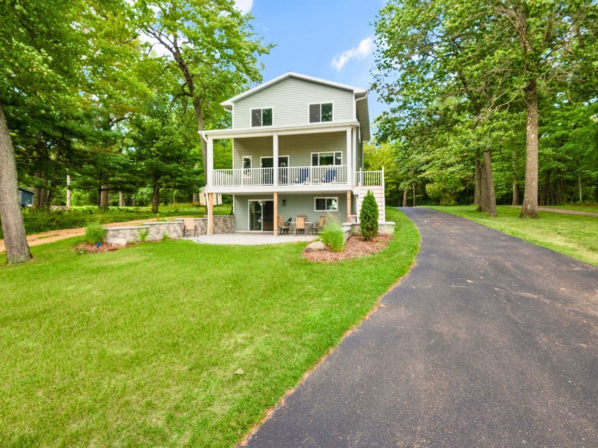 A large white house with a driveway leading to it is surrounded by trees.