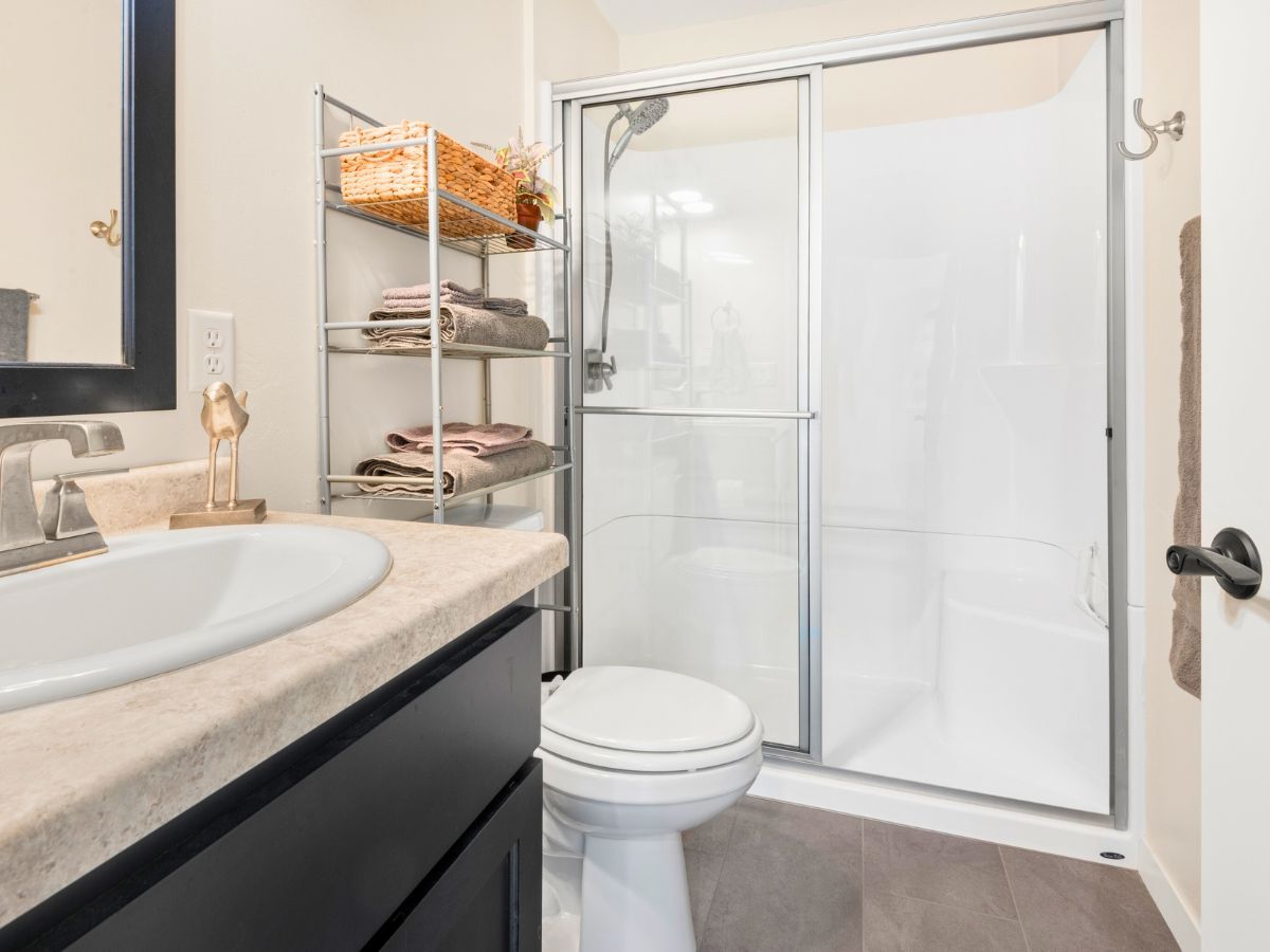 A bathroom with a toilet , sink , mirror and shower stall.