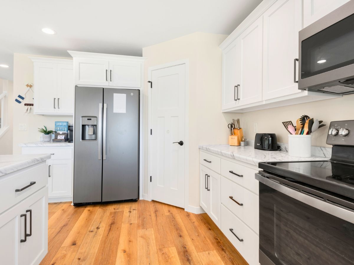 A kitchen with white cabinets , a stainless steel refrigerator , a stove , and a microwave.