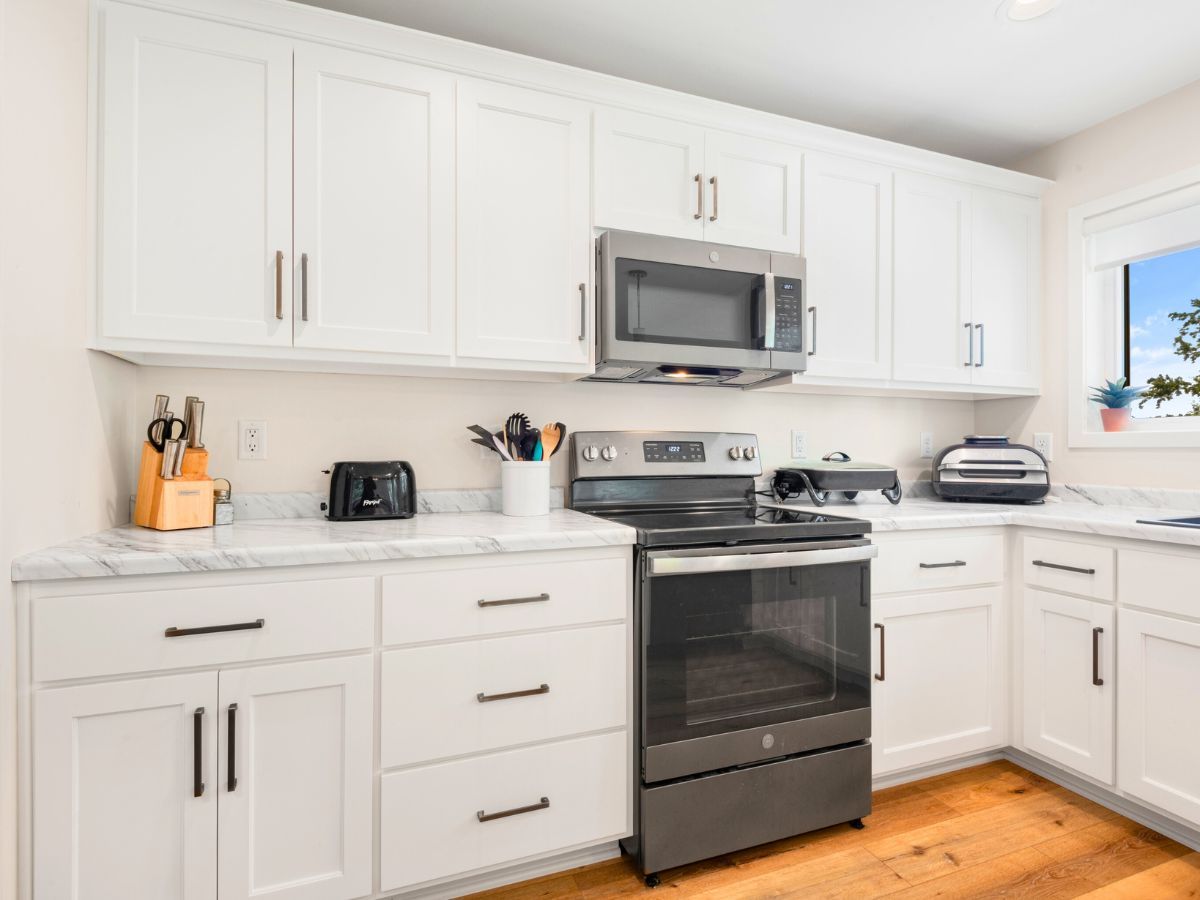 A kitchen with white cabinets , stainless steel appliances , and a window.