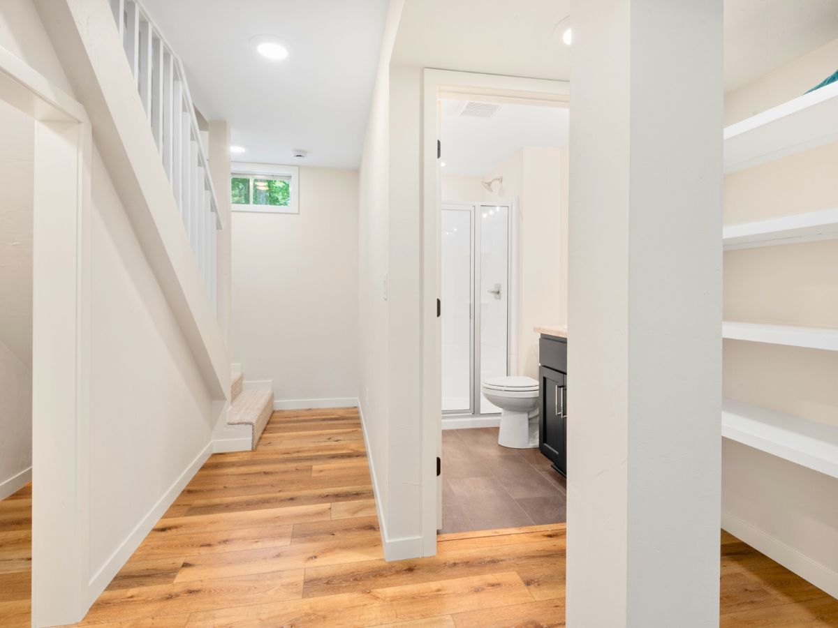 A hallway with hardwood floors leading to a bathroom and stairs.