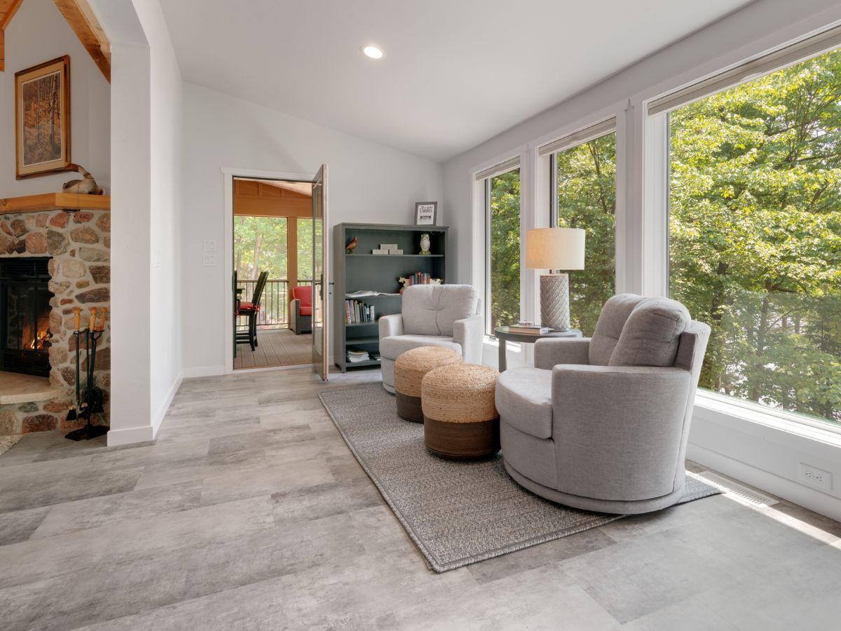 A living room with a fireplace , chairs , ottomans and lots of windows.