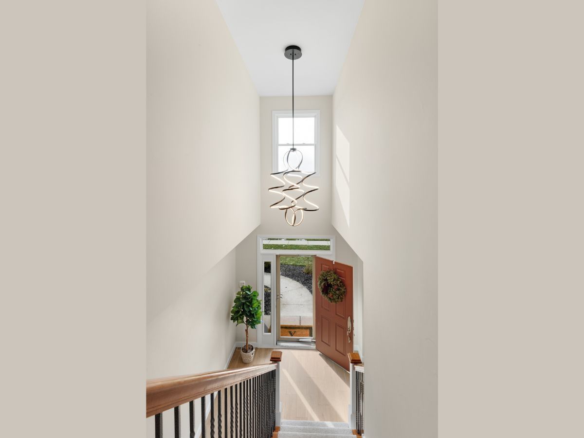 A staircase leading up to the front door of a house with a chandelier hanging from the ceiling.