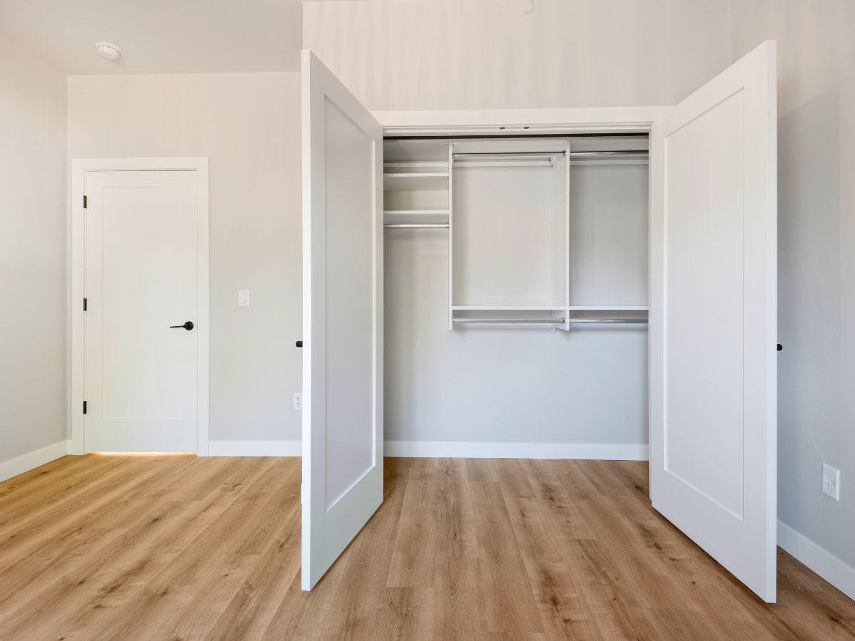 An empty bedroom with hardwood floors and a walk in closet with the doors open.