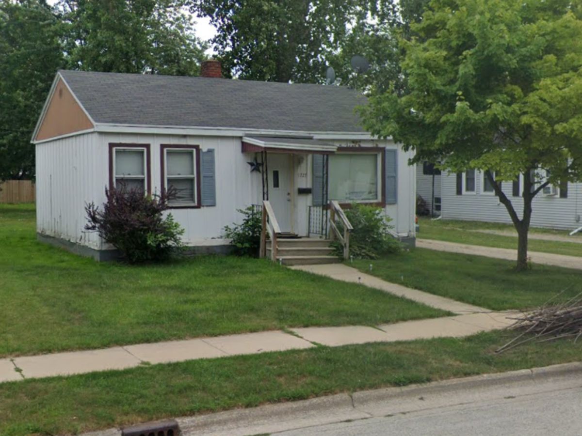 A small white house with a gray roof and a tree in front of it.