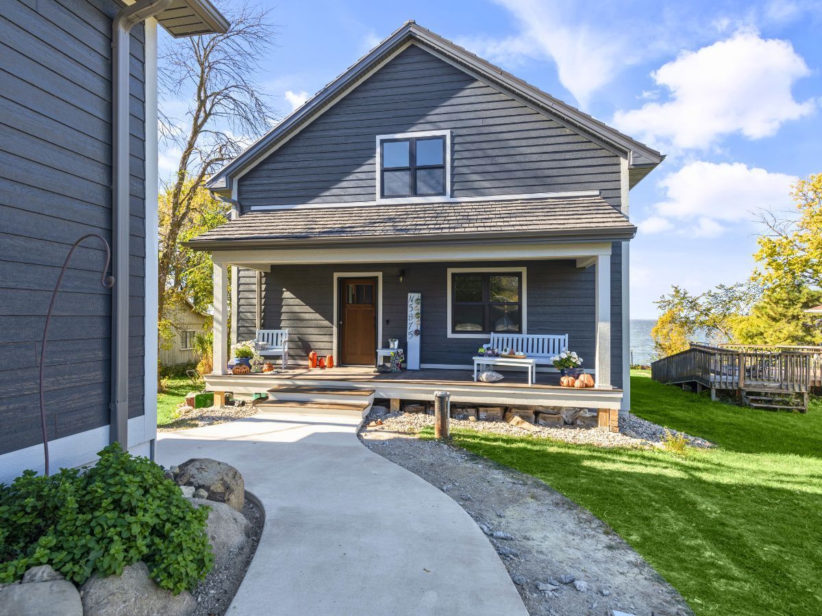 A gray house with a porch and a concrete walkway leading to it.