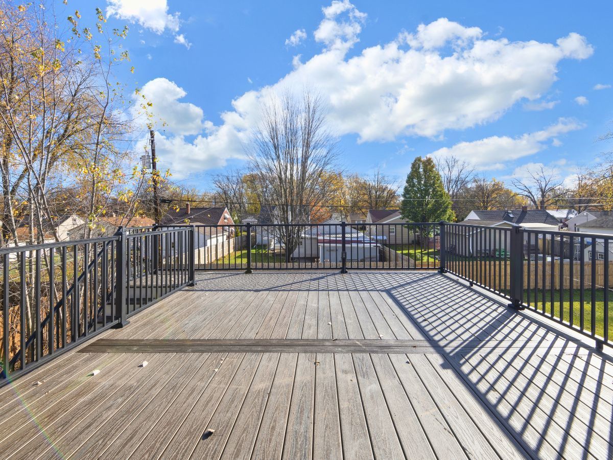 An empty wooden deck with a metal railing and a blue sky in the background.