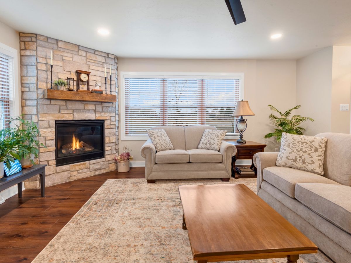 A living room with a couch , coffee table , fireplace and a ceiling fan.