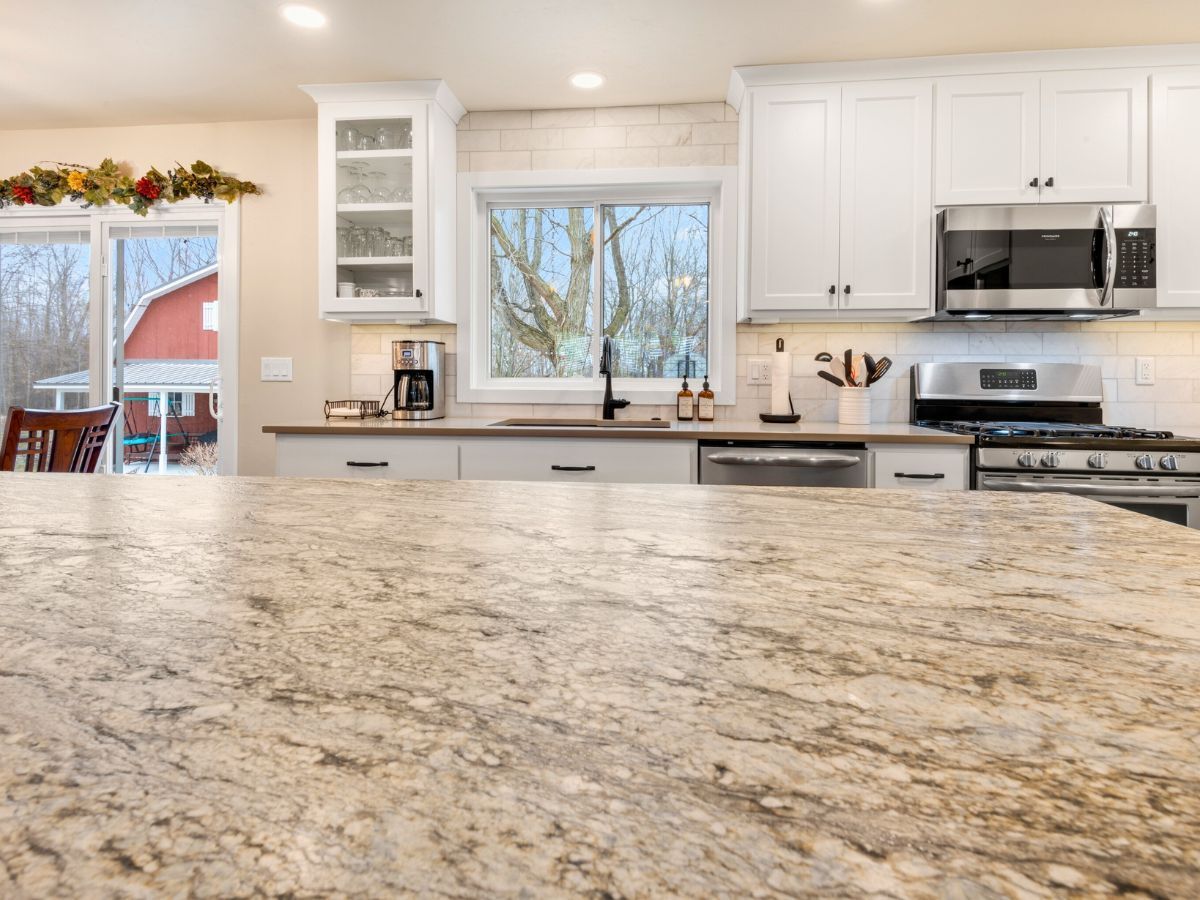 A kitchen with granite counter tops , white cabinets , stainless steel appliances and a large window.
