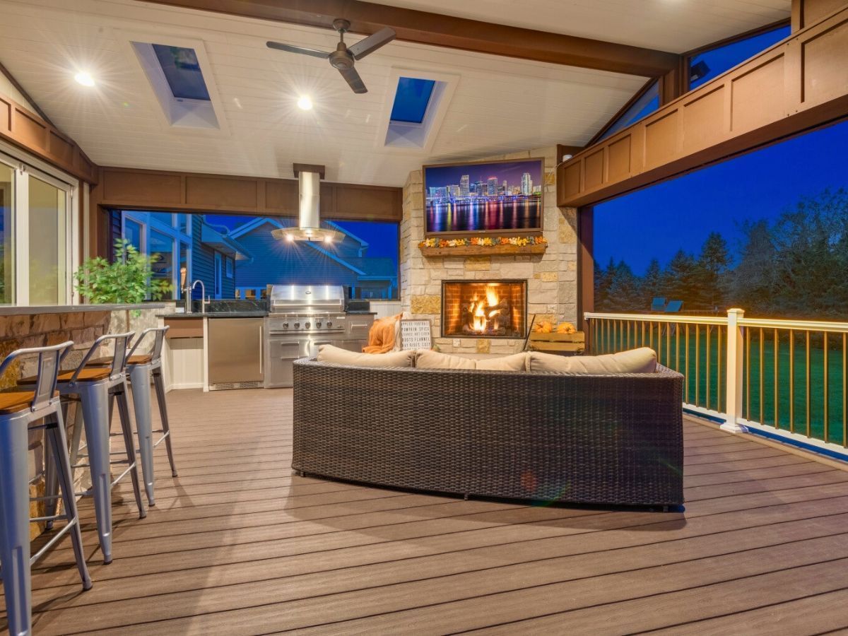 A patio with a fireplace , couch , stools and a television.