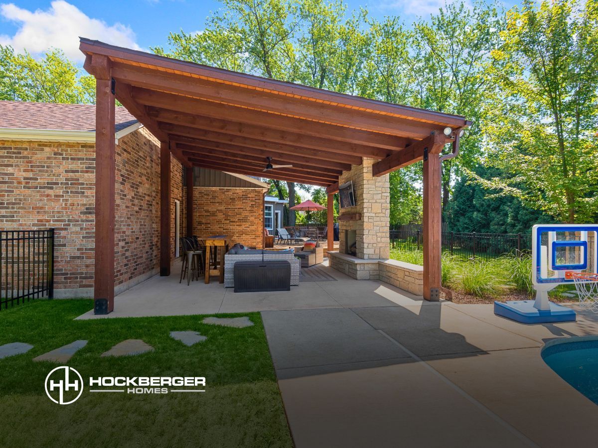 A patio with a wooden pergola and a fireplace in the backyard of a house.