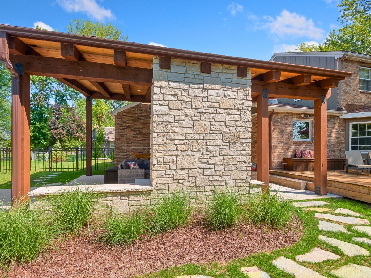 A stone building with a wooden roof is in the backyard of a house.