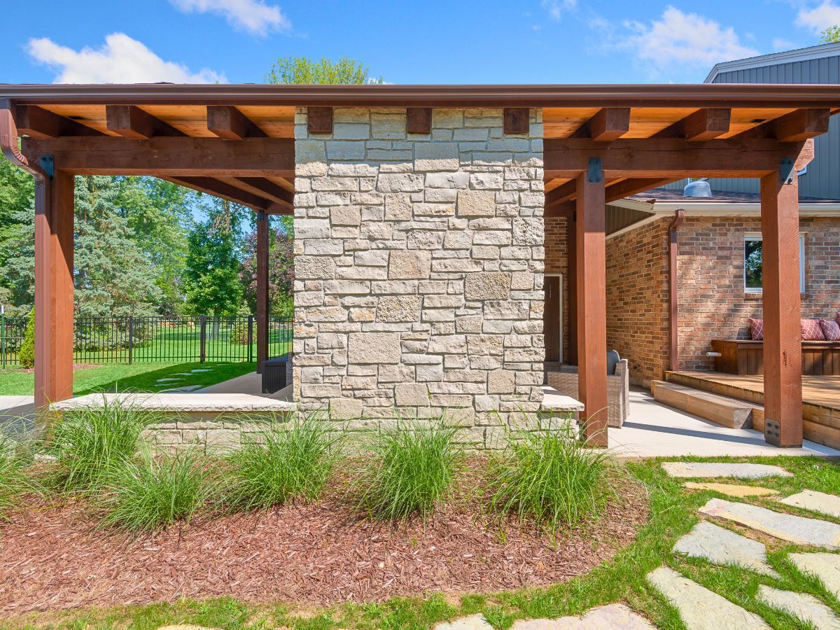 A wooden pergola is sitting in front of a stone building.