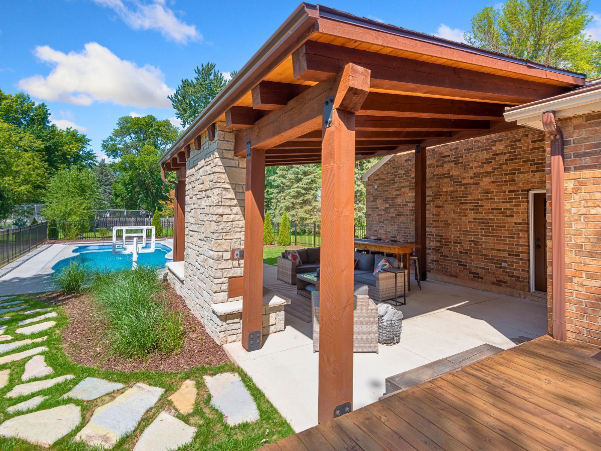 A patio with a wooden pergola and a swimming pool in the background.