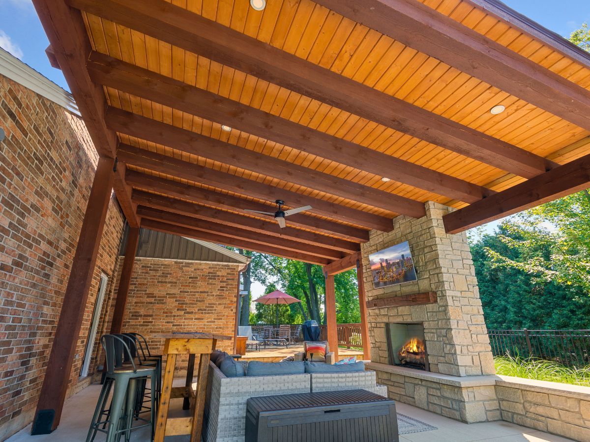 A covered patio with a fireplace and a wooden ceiling.