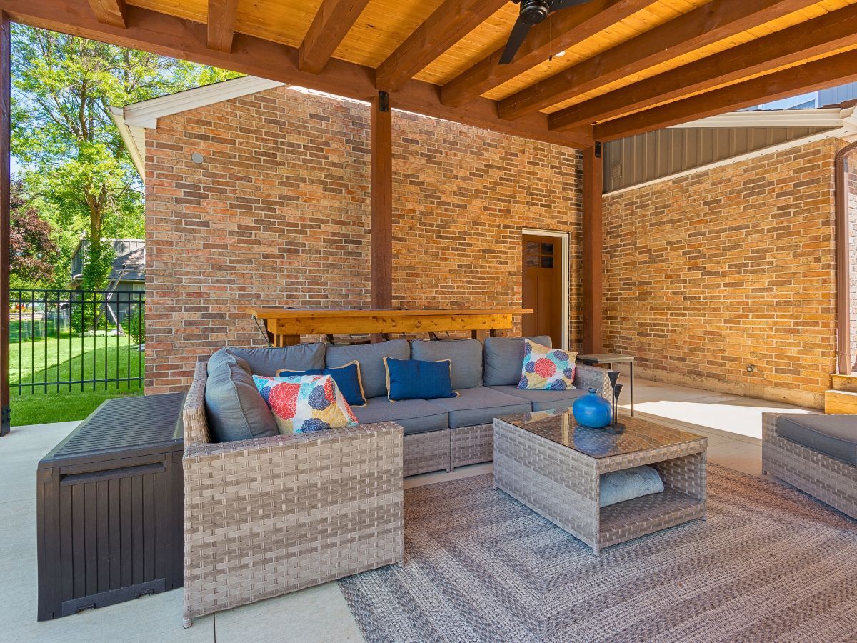 A patio with a couch , chairs , and a coffee table under a wooden roof.