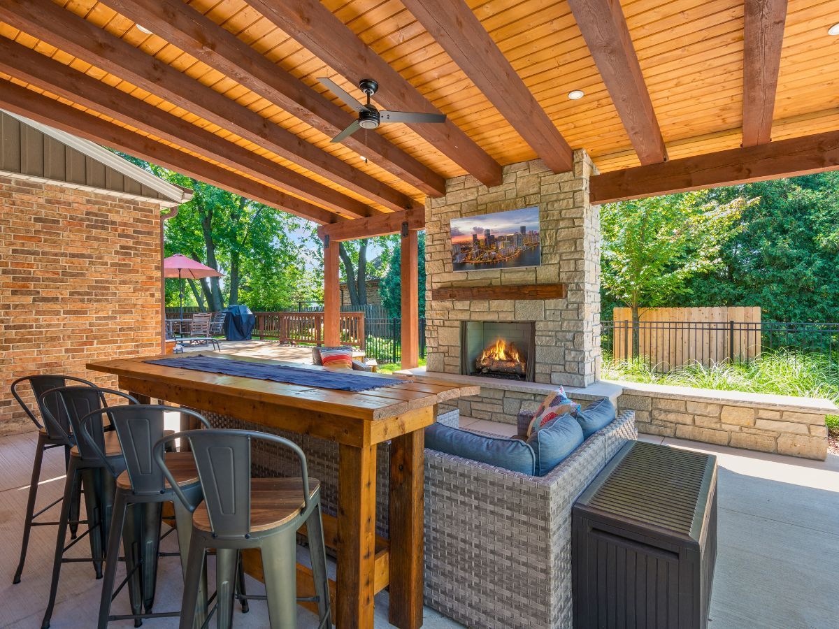 A patio with a fireplace , table and chairs under a wooden roof.