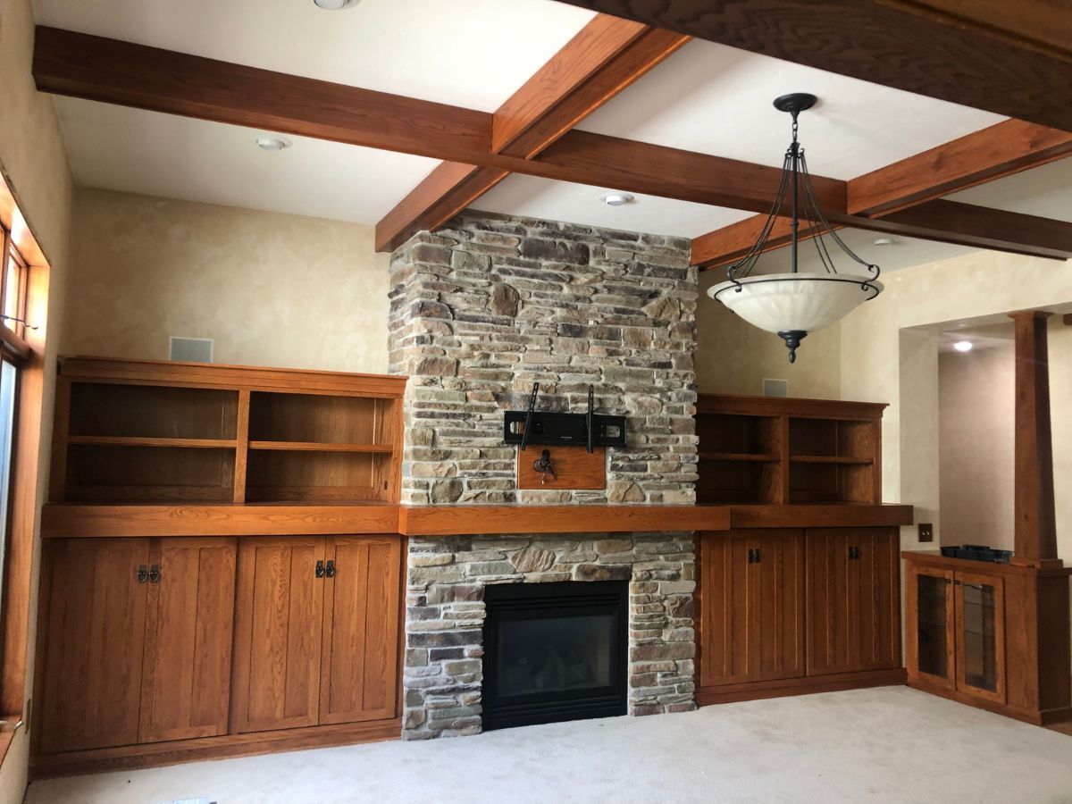 A living room with a stone fireplace and wooden cabinets