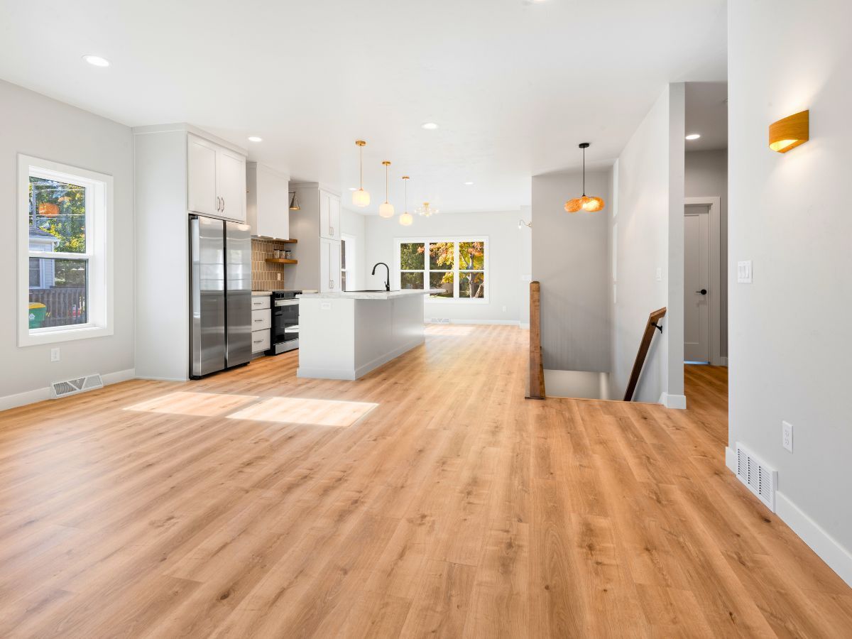 A living room with hardwood floors and a kitchen in the background.