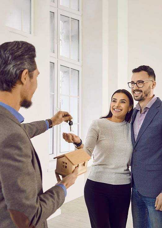 Realtor handing house keys to smiling couple in a bright entryway