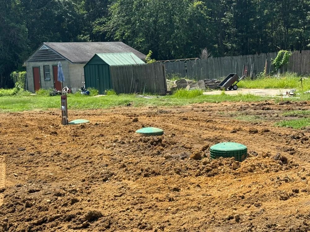 Rural yard with a small shed, green fence, and several green utility caps in a dirt field