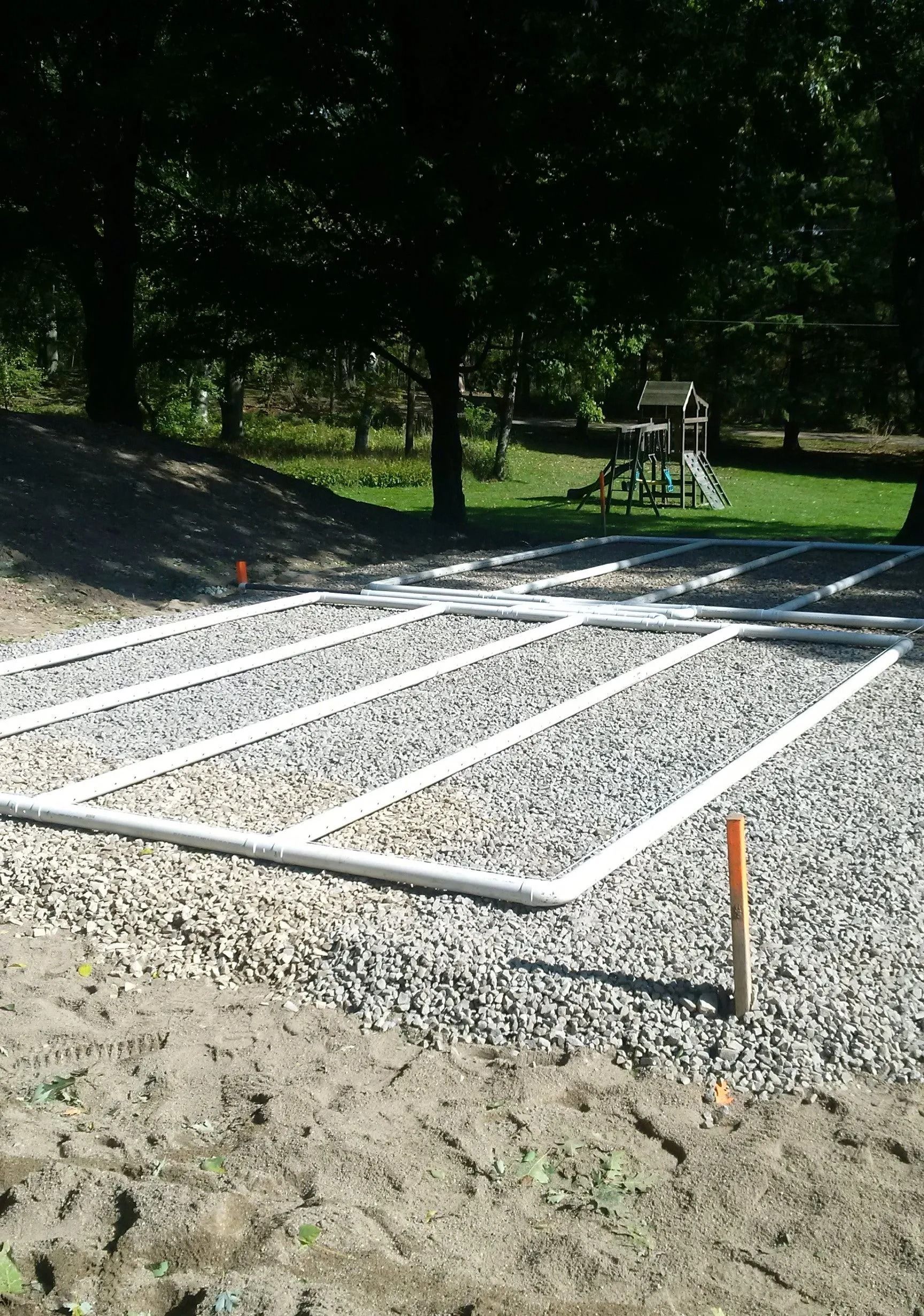 Gravel foundation with white rectangular framing in a wooded outdoor area, likely a construction site
