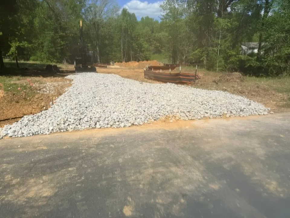 Large white gravel pile beside a paved road in a wooded area with construction materials nearby