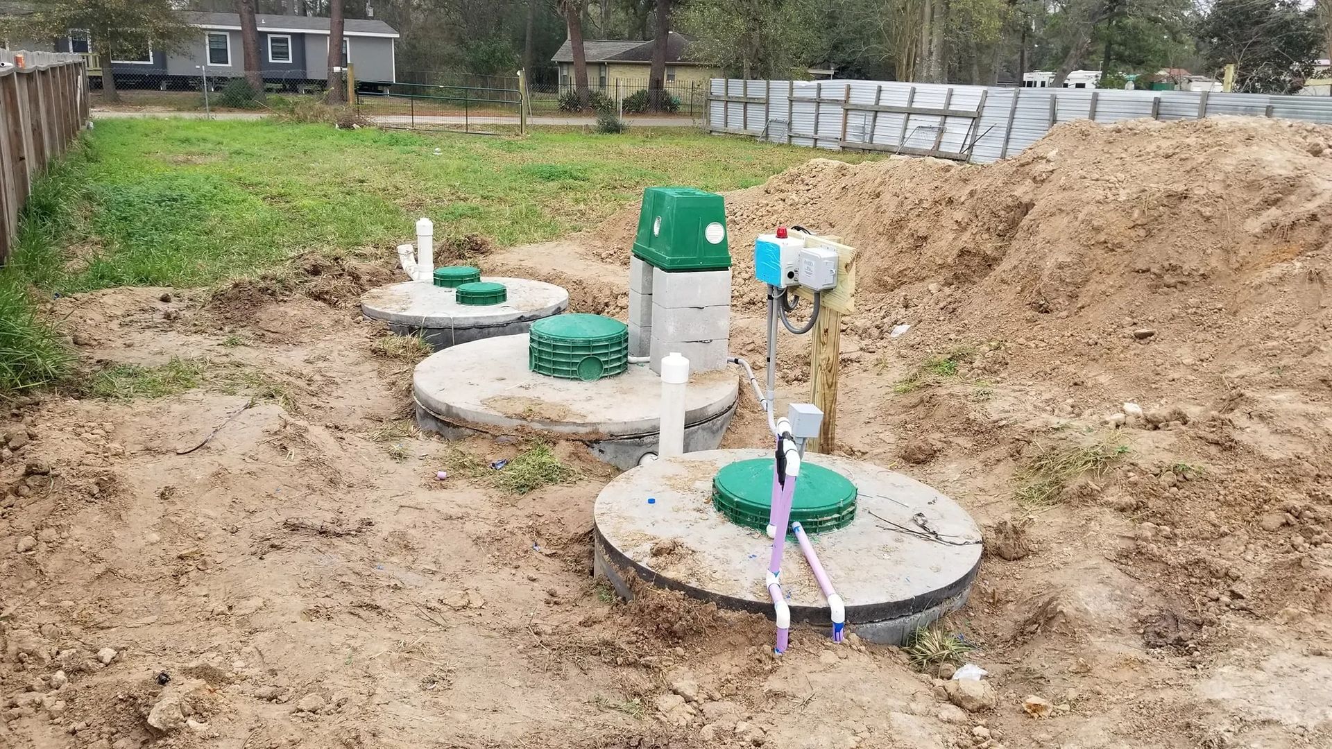 Outdoor utility installation with several white circular access lids and exposed pipes in a dirt yard