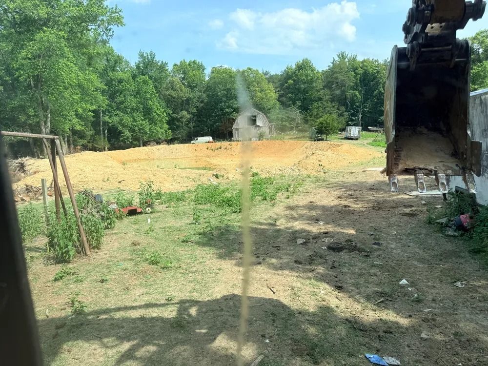 Construction site with excavator arm, dirt clearing, and trees under a blue sky