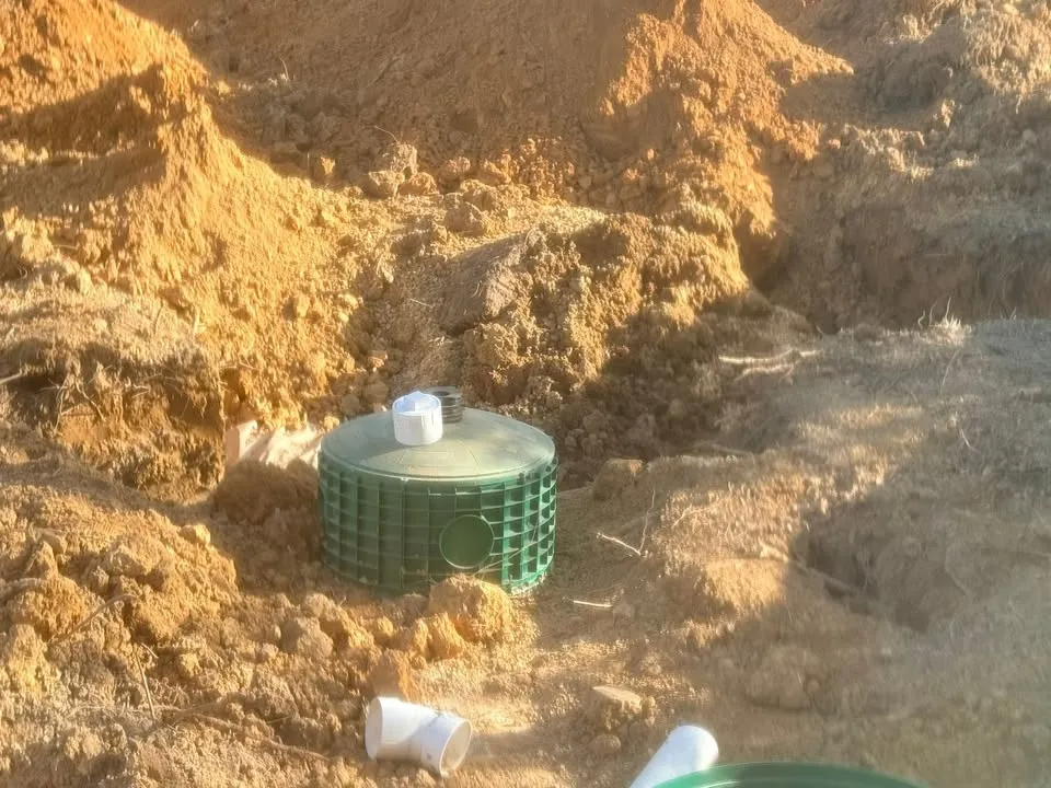 A green vent pipe in a muddy dirt trench with a small white cap on top.