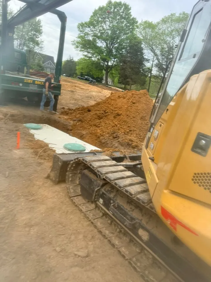 Yellow excavator beside a dirt pile at a muddy construction site, with another machine in the background