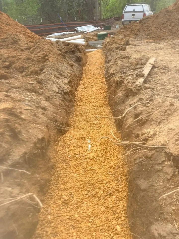 Fresh gravel in a narrow trench at a construction site, with a white van in the background.