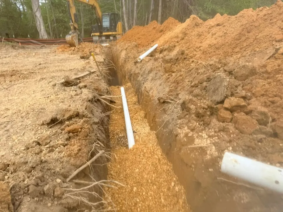A dirt trench beside a construction site with white PVC pipes running through it.