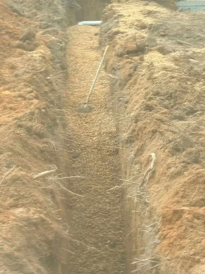 A narrow dirt trench in a dry field with a long metal rod leaning into it.