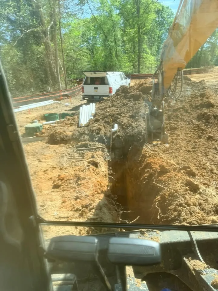 Excavator digging a trench at a wooded construction site beside a white utility truck