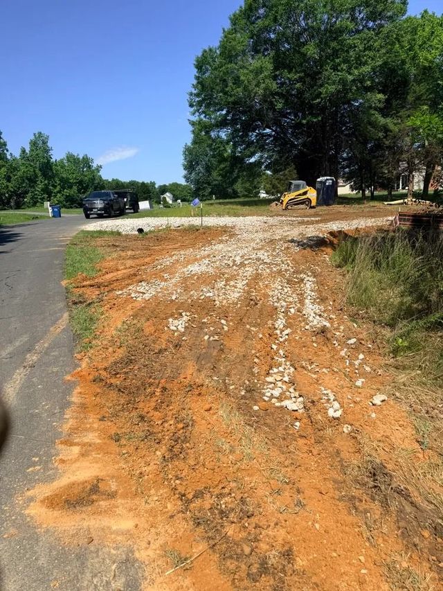 Roadside dirt excavation with a black SUV and backhoe near trees under a clear blue sky