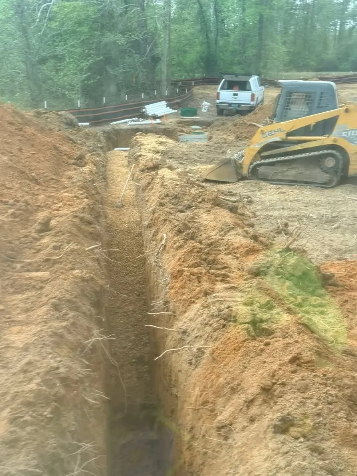 Construction trench beside excavator and white truck in a wooded worksite
