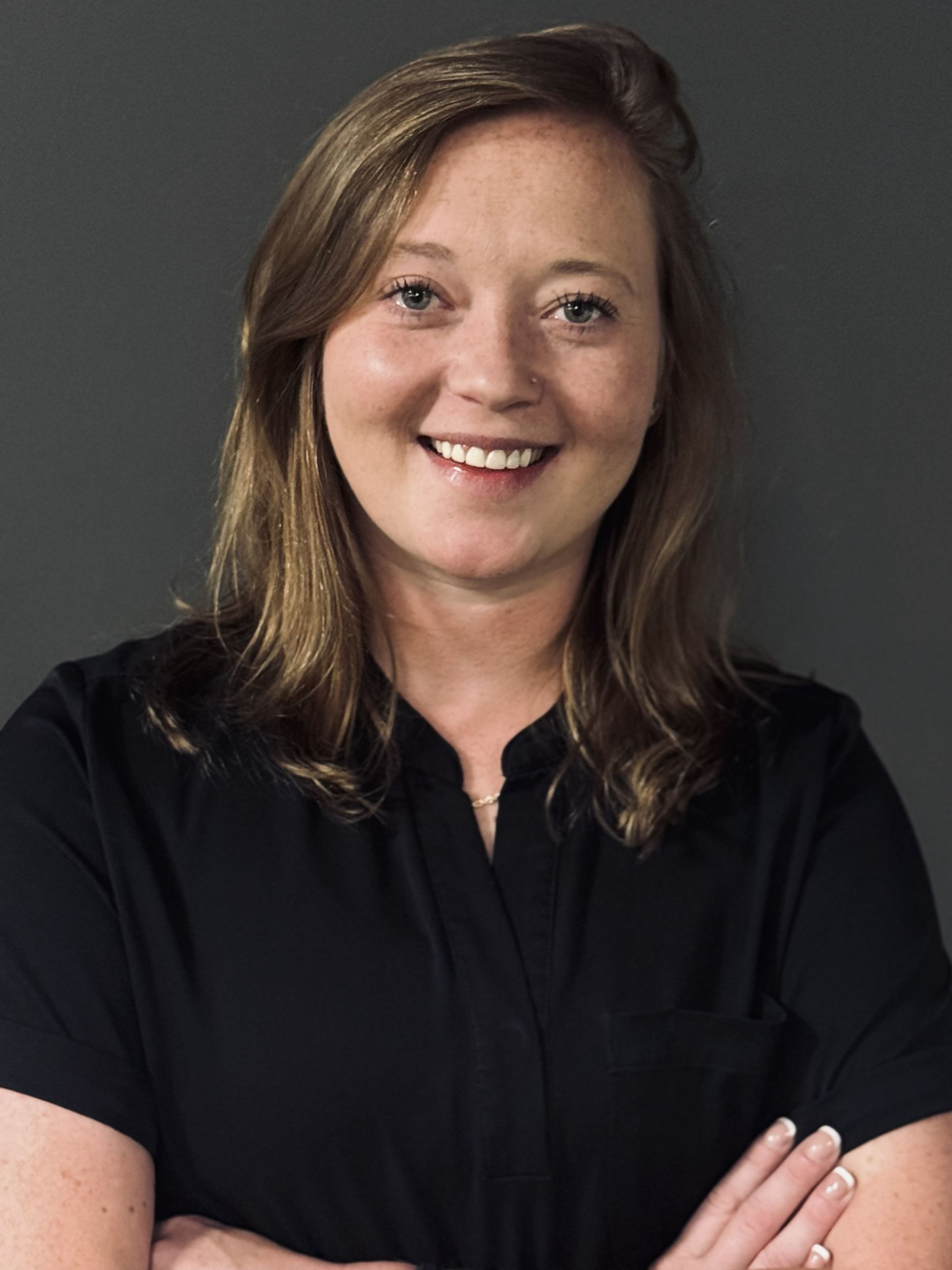 A woman wearing a black shirt and a necklace smiles for the camera.