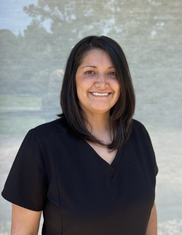 A woman in a black scrub top is smiling for the camera.