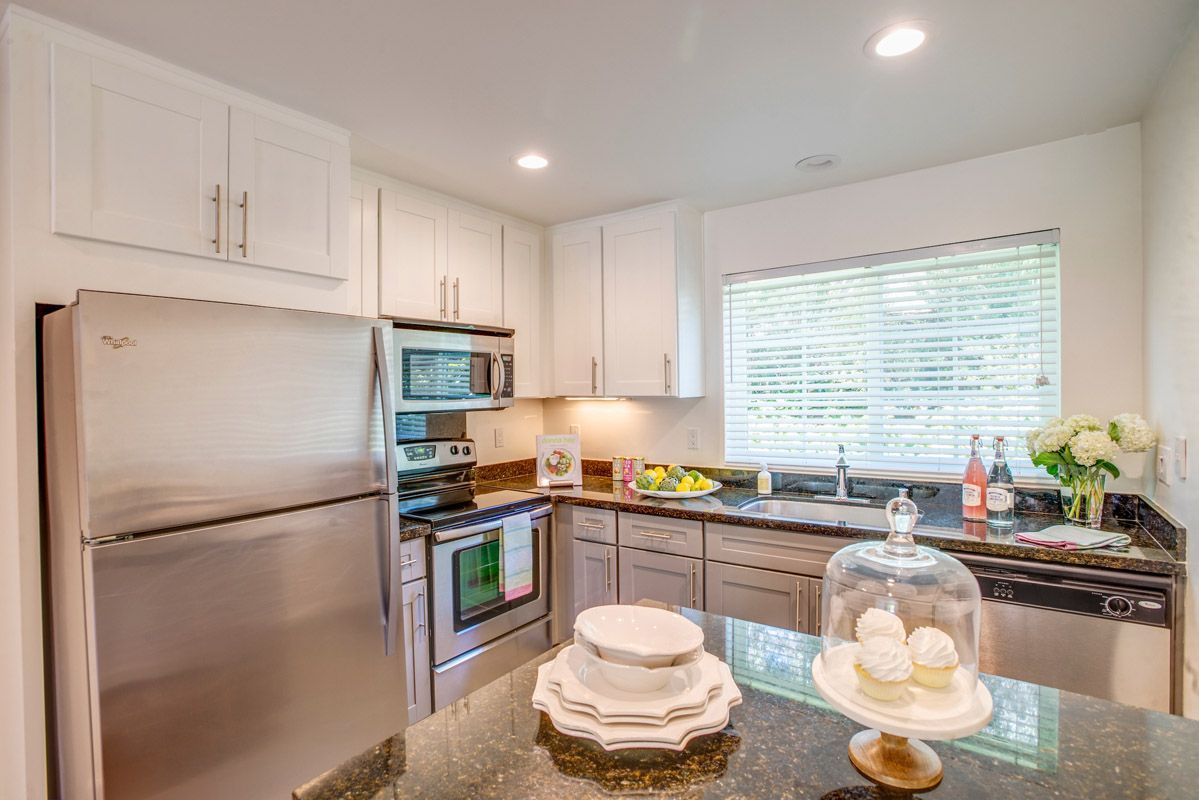 Bright modern kitchen with white cabinets, stainless appliances, and a large window.