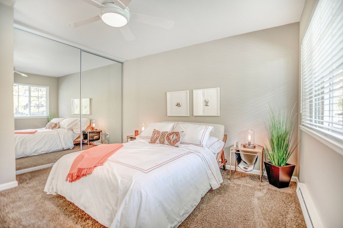 Bedroom with a neatly made bed, mirrored closet doors, two nightstands, and a potted plant.